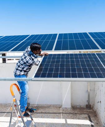 Indian worker installing solar panels on roof of house. Maintenance of photovoltaic panel system. Concept of alternative, renewable energy.